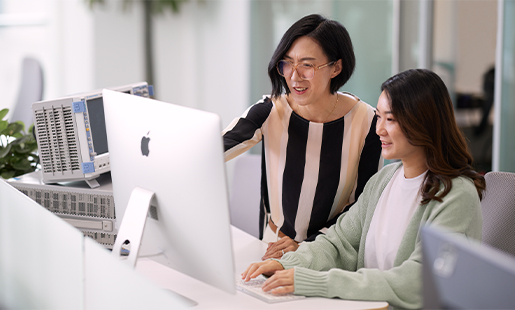 Ella de pie junto a una persona de su equipo que está sentada delante de una pantalla de Apple.