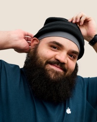 Portrait d’un membre de l’équipe Apple Retail souriant, avec une barbe fournie et un bonnet en laine.