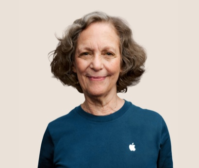Portrait d’un membre de l’équipe Apple Retail souriant, avec des cheveux gris foncé et ondulés.