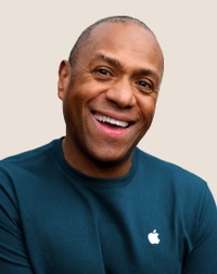 Portrait d’un membre de l’équipe Apple Retail souriant, avec des cheveux gris foncé et courts.