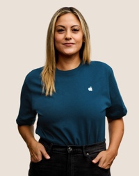 Portrait d’un membre de l’équipe Apple Retail souriant, avec de longs cheveux blond foncé.