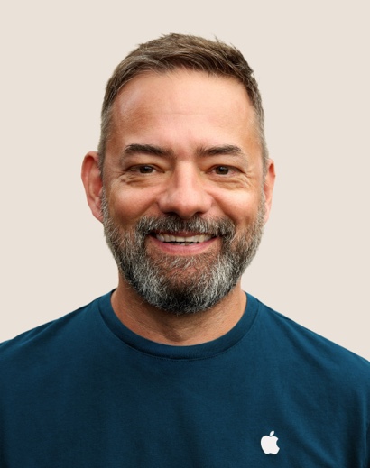 Portrait d’un membre de l’équipe Apple Retail souriant, avec des cheveux gris courts et une barbe.