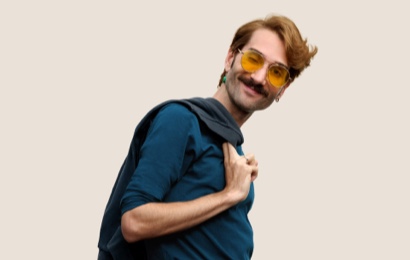 Portrait d’un membre de l’équipe Apple Retail souriant, avec des cheveux courts blond foncé et des lunettes.