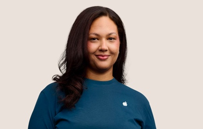 Portrait d’un membre de l’équipe Apple Retail souriant, avec de longs cheveux de couleur foncée.