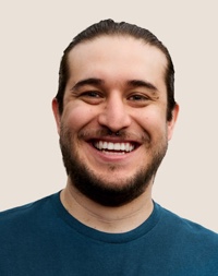 Portrait d’un membre de l’équipe Apple Retail souriant, avec des cheveux de couleur foncée et une barbe.