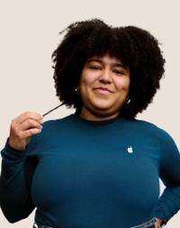 Portrait d’un membre de l’équipe Apple Retail souriant, avec de longs cheveux bouclés de couleur foncée.