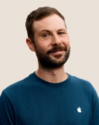 Portrait d’un membre de l’équipe Apple Retail souriant, avec des cheveux de couleur foncée et une barbe.