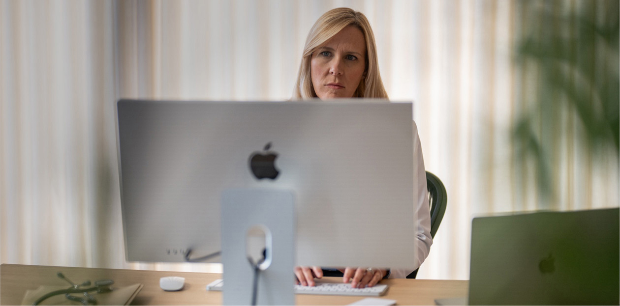 En vårdgivare vid ett skrivbord som tittar på en Mac-skärm.