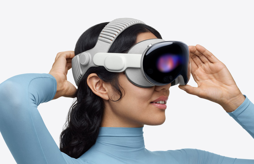 Personne portant un Apple Vision Pro, assemblé avec bandeau tissé à sangle double, sangle supérieure placée au sommet de la tête, une main posée sur la sangle inférieure à l’arrière de la tête, l’autre posée sur la monture en alliage d’aluminium