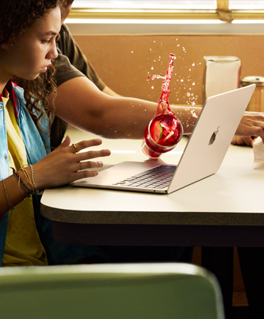 Une personne tente d’attraper un objet dans un restaurant et renverse une boisson glacée sur un MacBook ouvert
