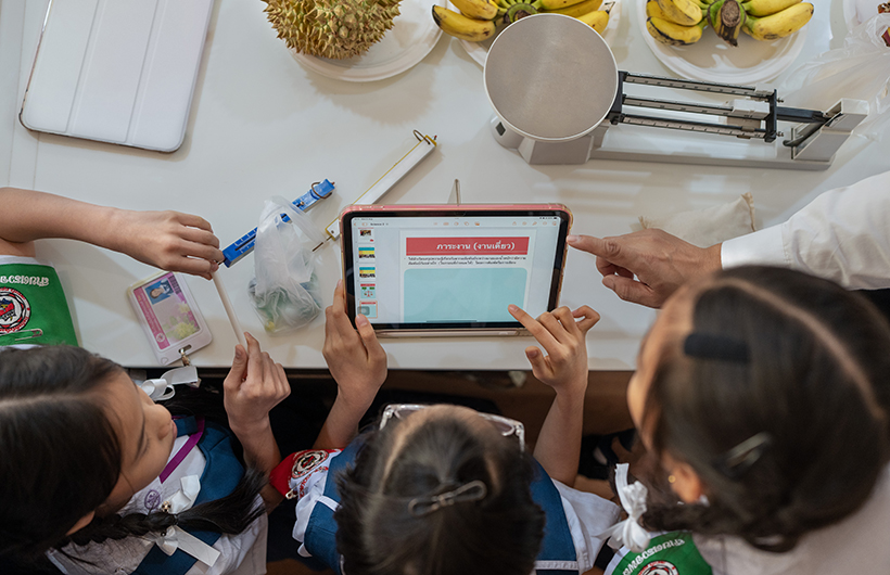 Tre studentesse della scuola primaria riunite attorno a un iPad per collaborare a una presentazione per un progetto di scienze.