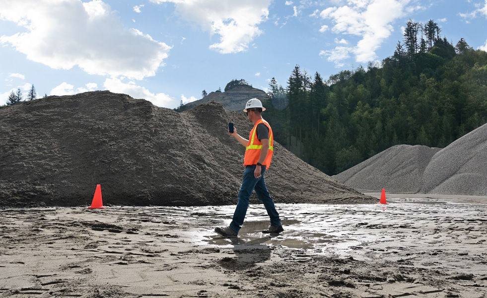 Un agent de terrain évalue un chantier avec un iPhone tout en traversant un sol boueux