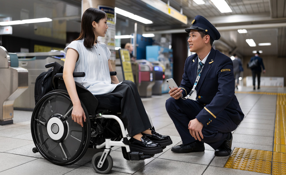 Conversation entre une femme en tenue professionnelle dans un fauteuil roulant et un agent de station sur le quai.