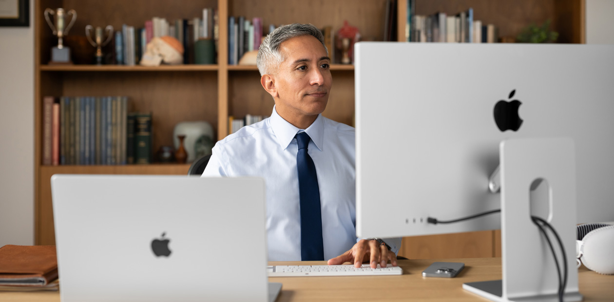 Un prestataire assis à son bureau derrière des écrans d’iMac et de MacBook Pro.