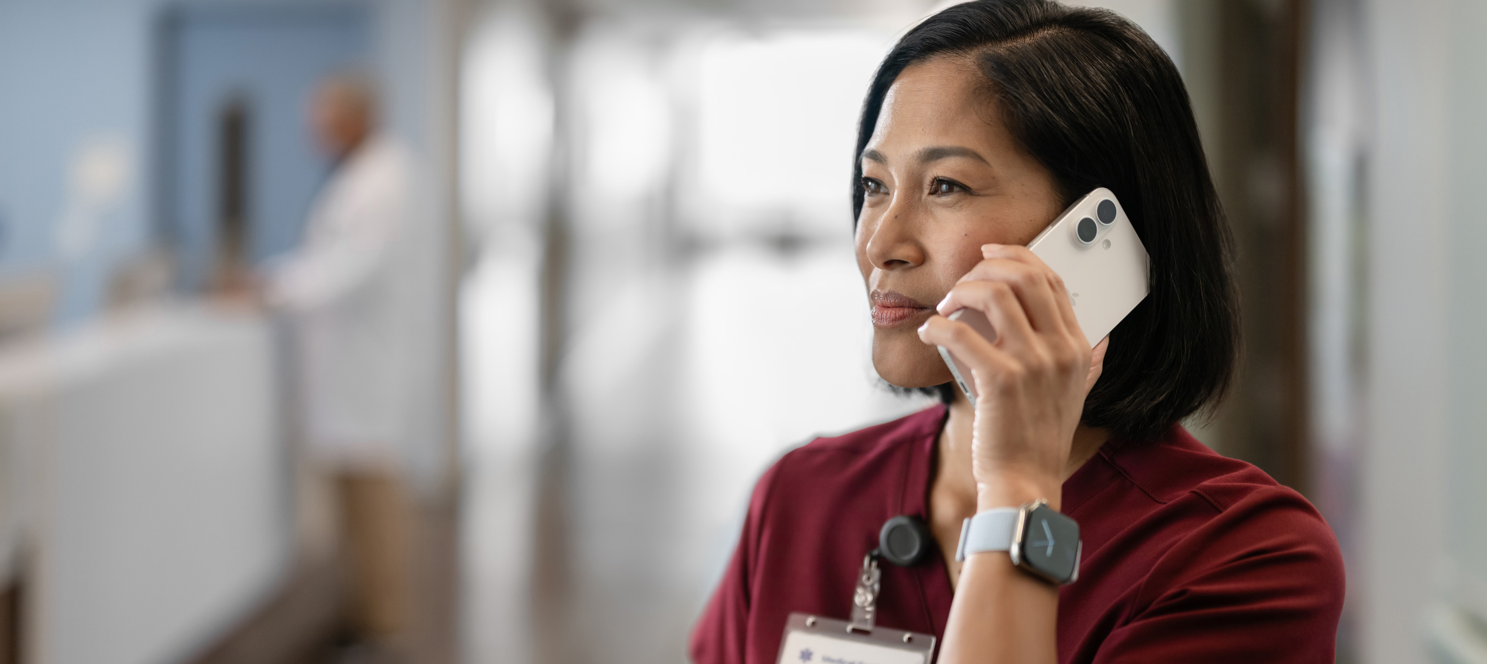 Une infirmière en blouse rouge parle sur son iPhone.