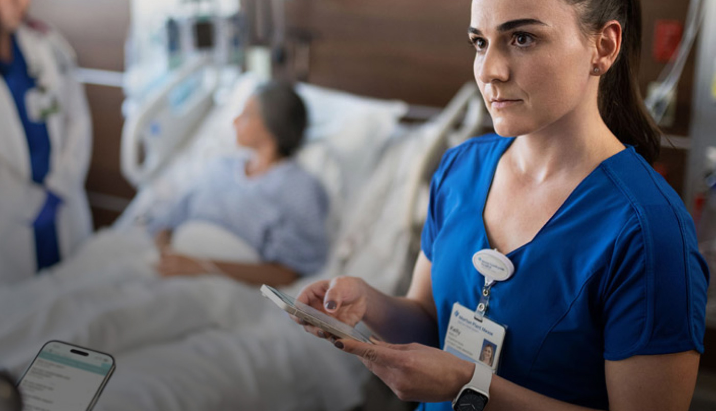 En sjuksköterska skickar ett meddelande på sin iPhone medan en annan vårdgivare pratar med en patient.