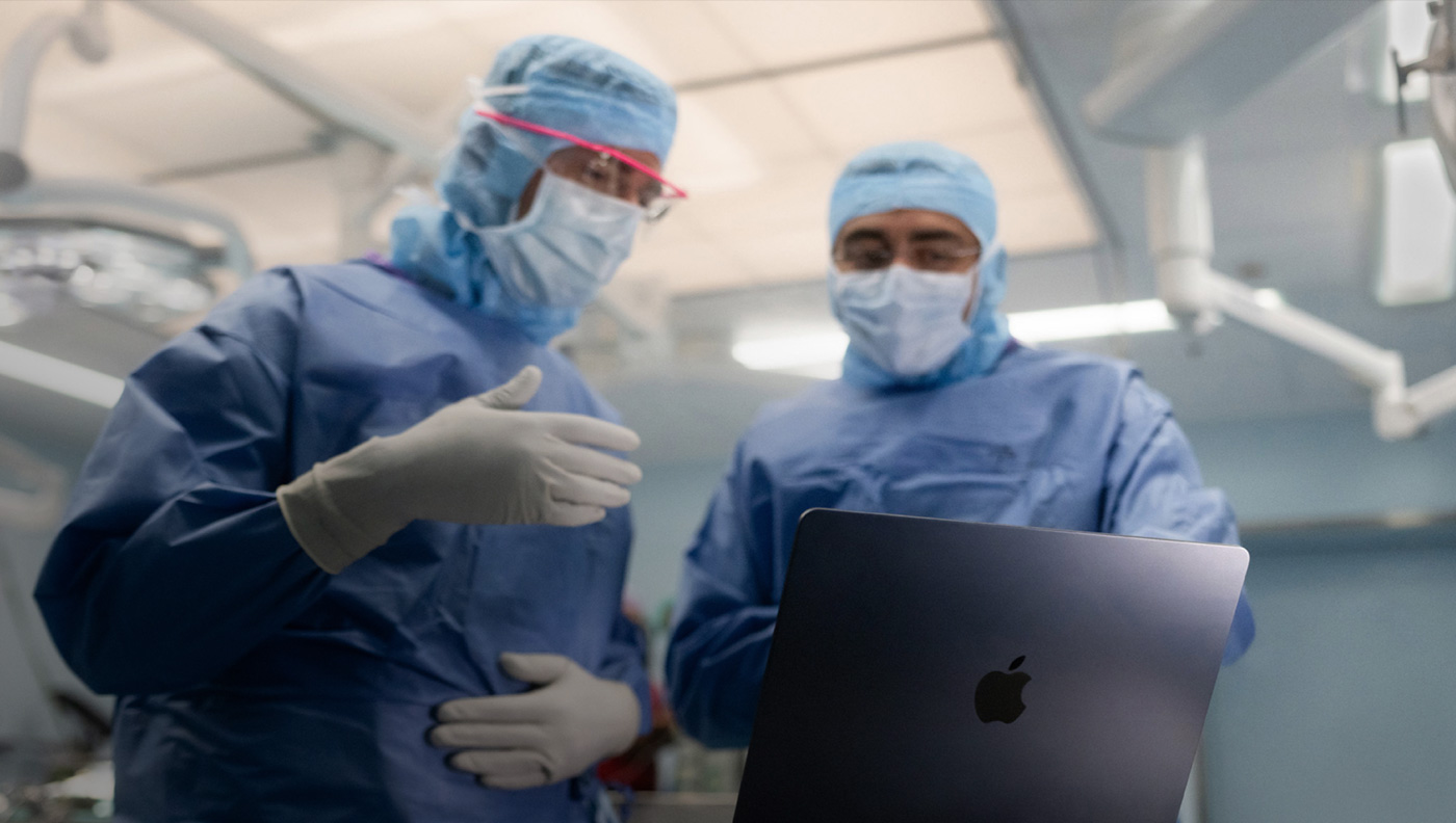 Två kirurger diskuterar något på skärmen på en MacBook Pro på operationsavdelningen.