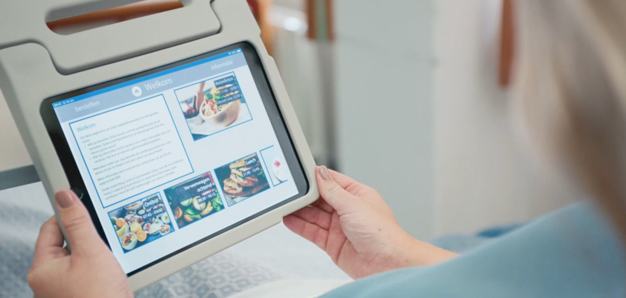 En patient sitter i sin sjukhussäng och tittar på en iPad-skärm.