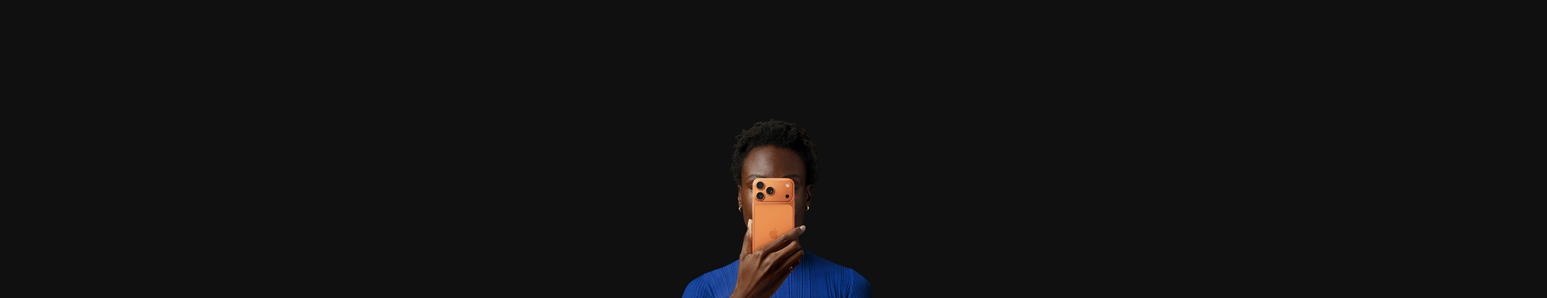 コズミックオレンジのiPhone 17 Proを顔の前で持っている人物。背面を外側に向けている