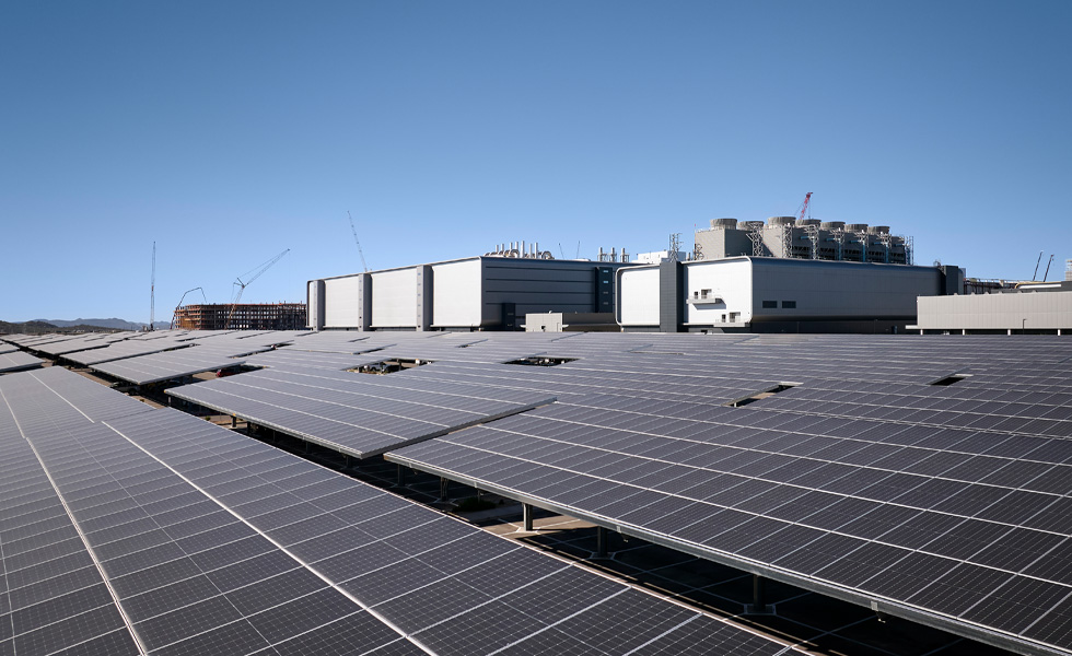 Rader med solpaneler installerade intill en industribyggnad under en klarblå himmel