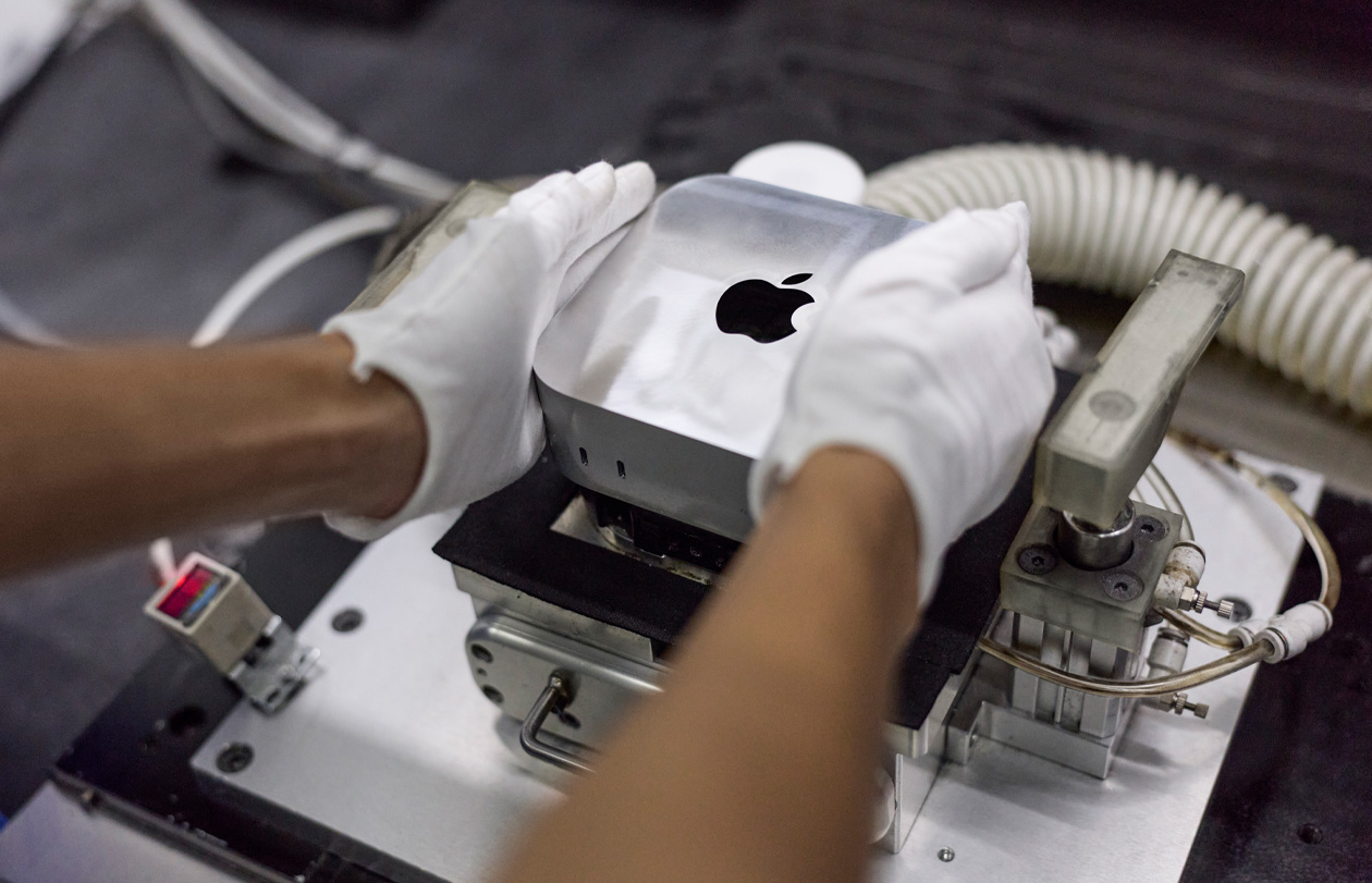 Händer i handskar placerar en Mac mini i en tillverkningsmaskin under montering