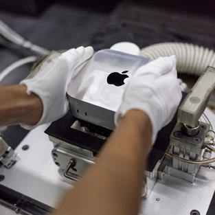 Händer i handskar placerar en Mac mini i en tillverkningsmaskin under montering