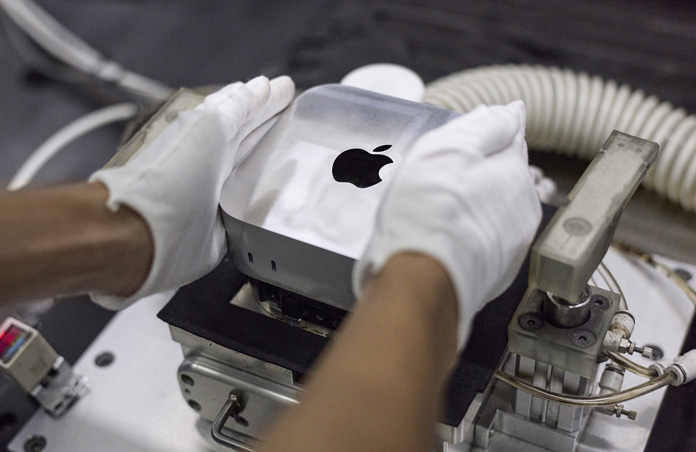 Händer i handskar placerar en Mac mini i en tillverkningsmaskin under montering