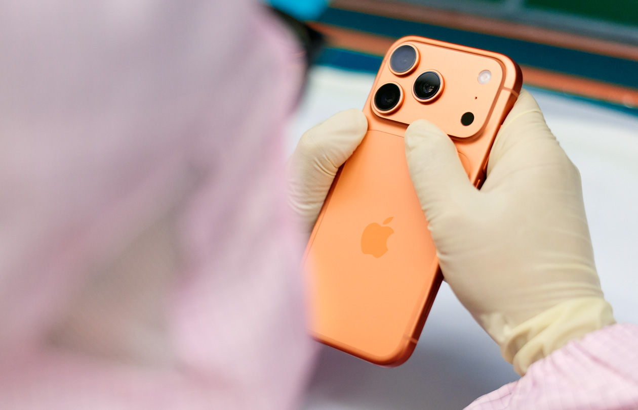 En medarbetare i heltäckande arbetskläder inspekterar en iPhone vid en arbetsstation