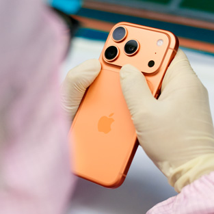 En medarbetare i heltäckande arbetskläder inspekterar en iPhone vid en arbetsstation