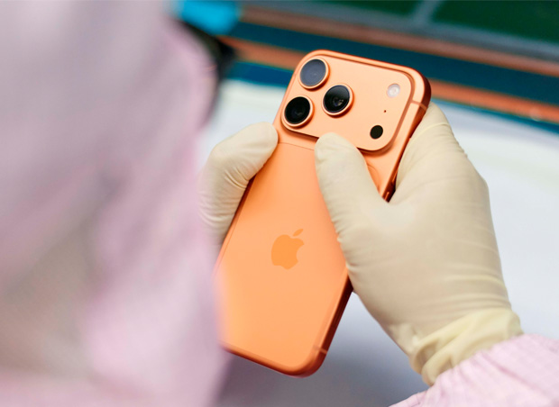 En medarbetare i heltäckande arbetskläder inspekterar en iPhone vid en arbetsstation